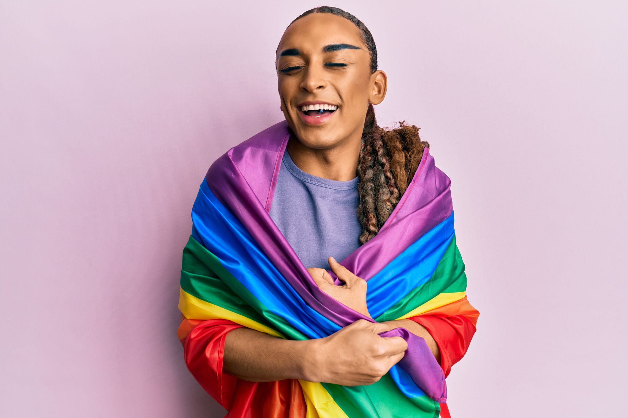 Pessoa sorrindo envolta em uma bandeira do orgulho LGBTQIA+